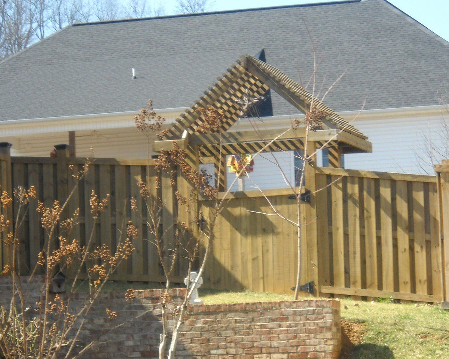 A wooden fence surrounds a brick wall in front of a house