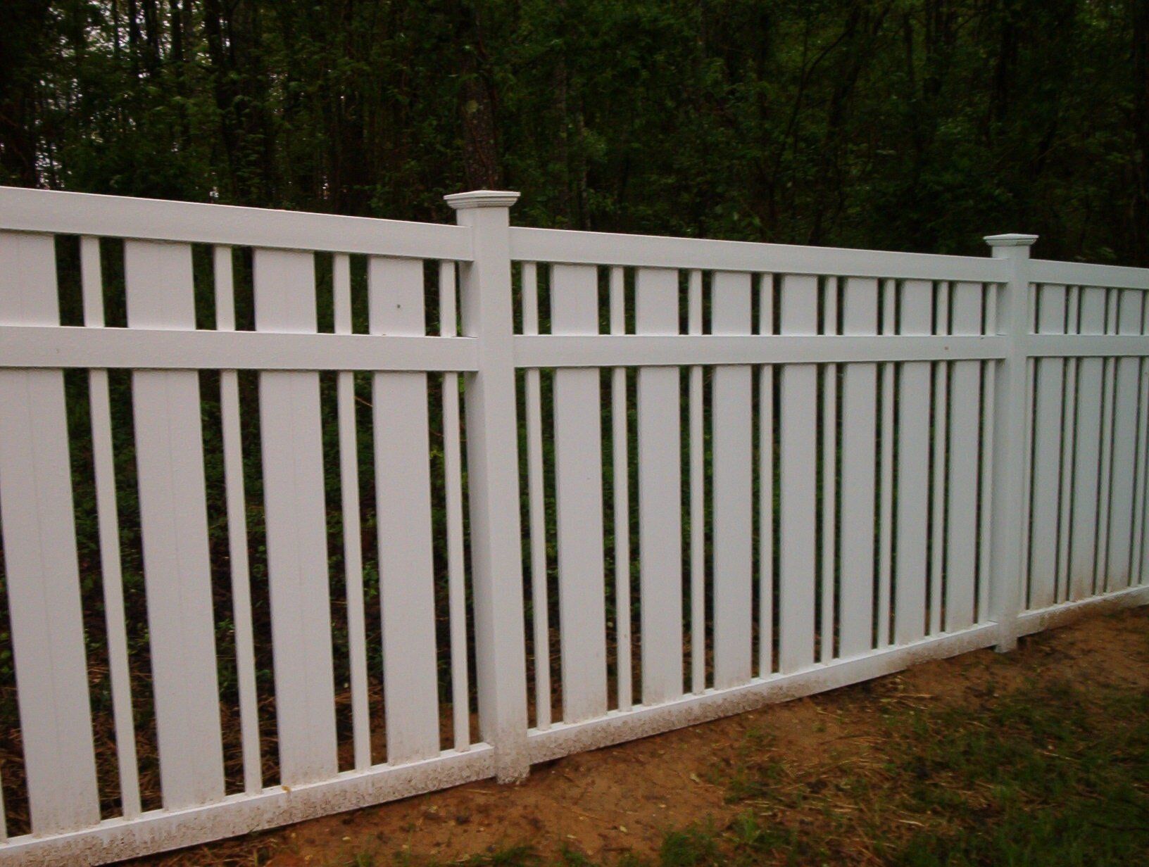 A white fence with black stripes is surrounded by grass and trees.