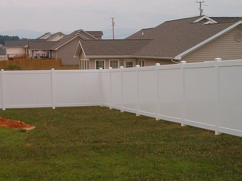 A white fence surrounds a lush green yard in front of a house.
