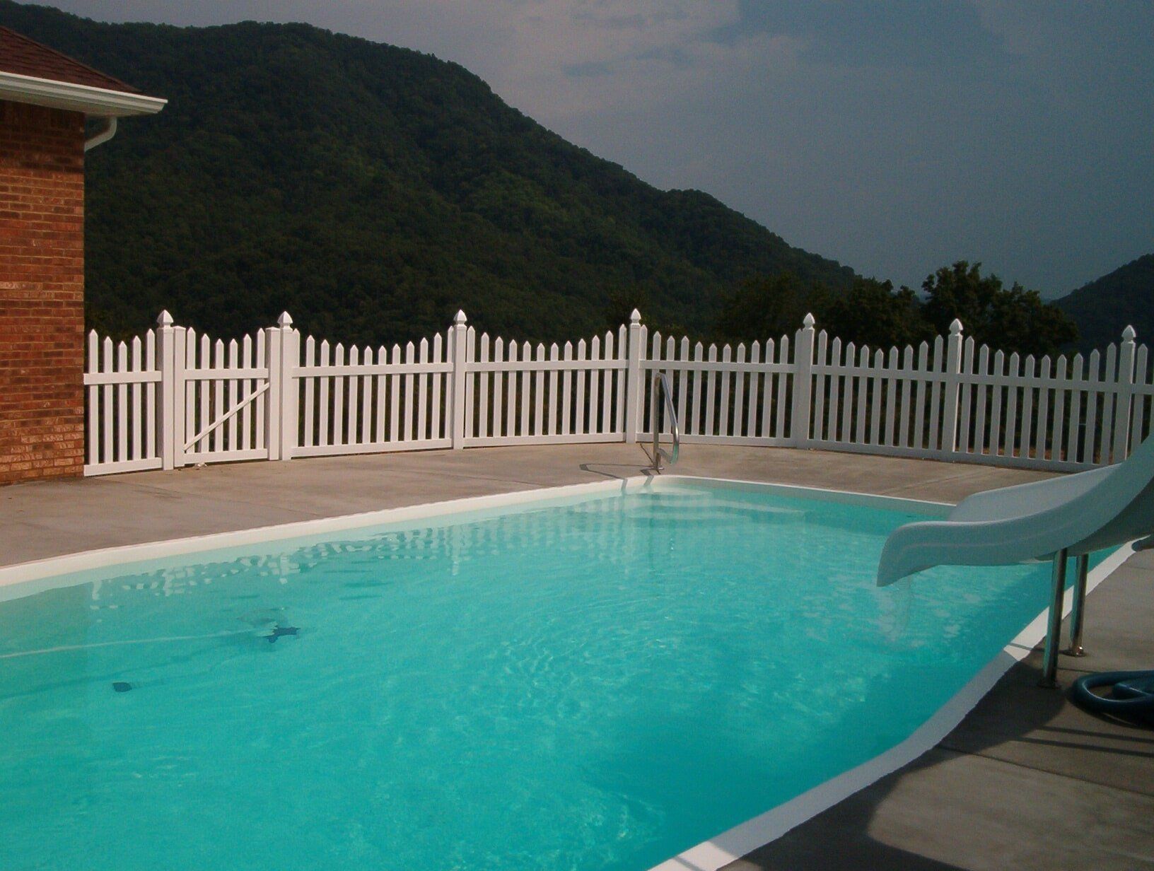 A swimming pool with a white picket fence and mountains in the background. A swimming pool with a white picket fence and mountains in the background.