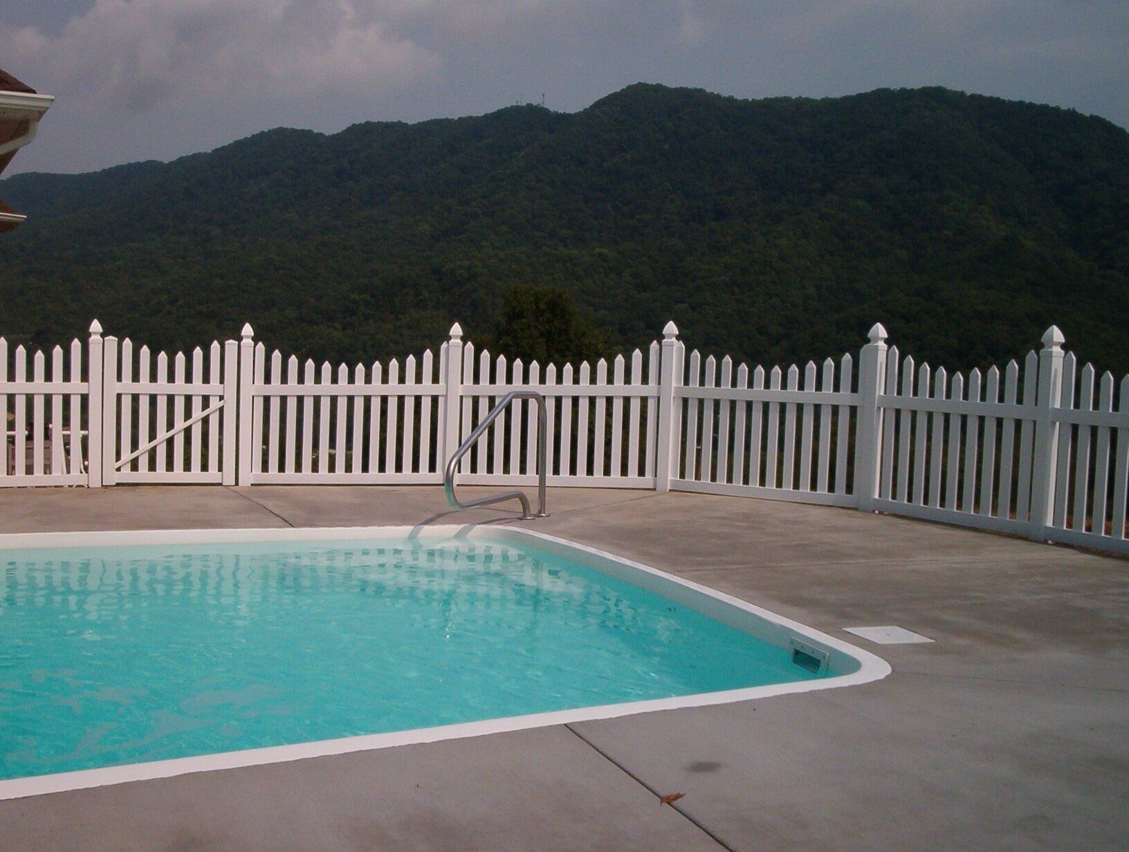 A swimming pool surrounded by a white picket fence with mountains in the background A swimming pool surrounded by a white picket fence with mountains in the background