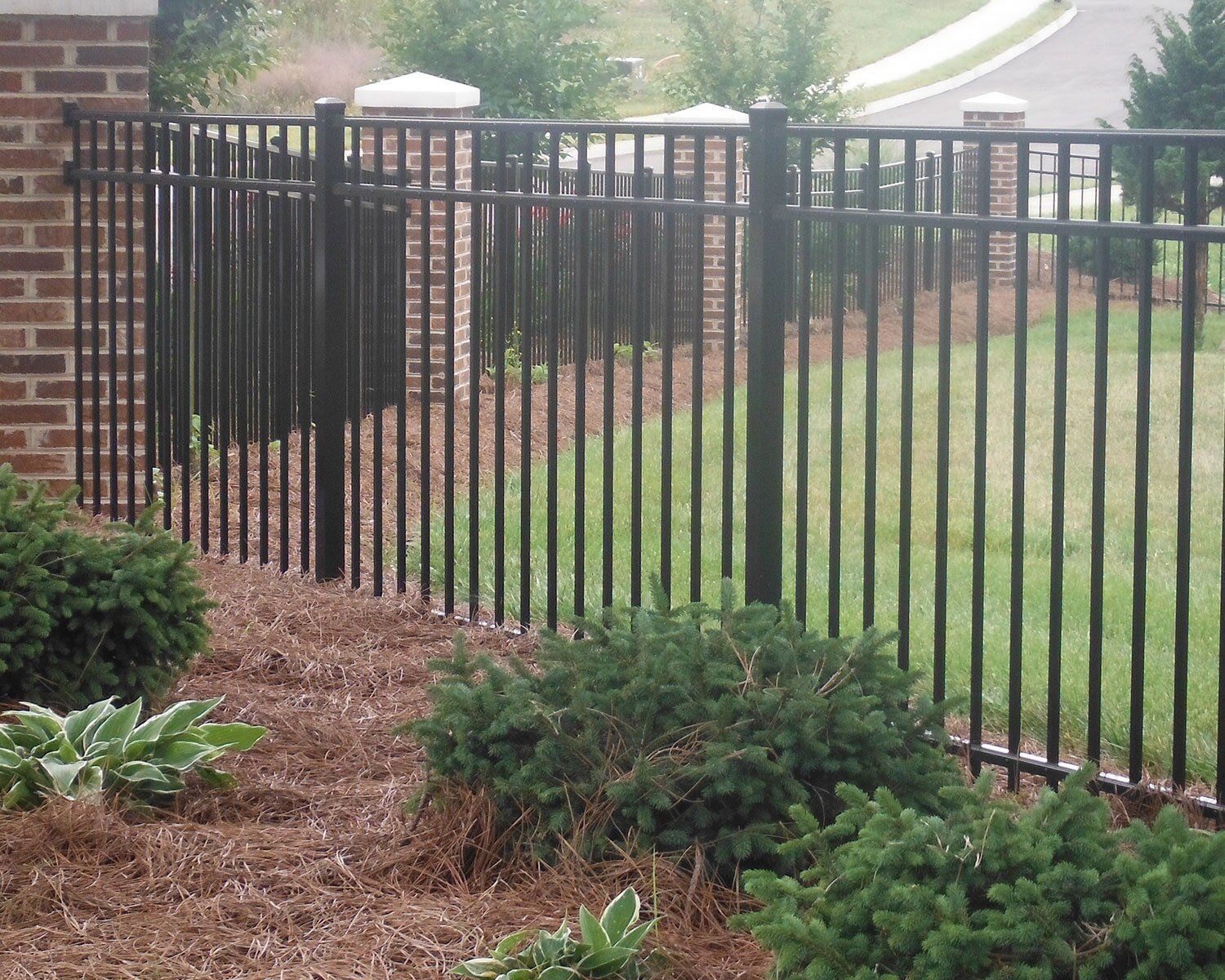 A black metal fence with a brick wall in the background A black metal fence with a brick wall in the background