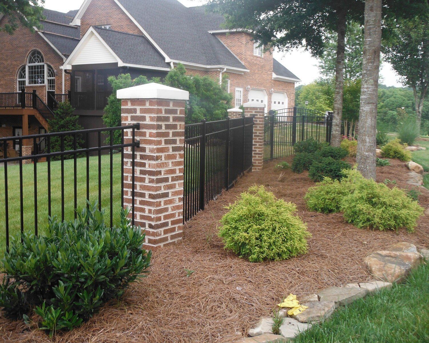 A black fence surrounds a brick pillar in front of a large brick house A black fence surrounds a brick pillar in front of a large brick house