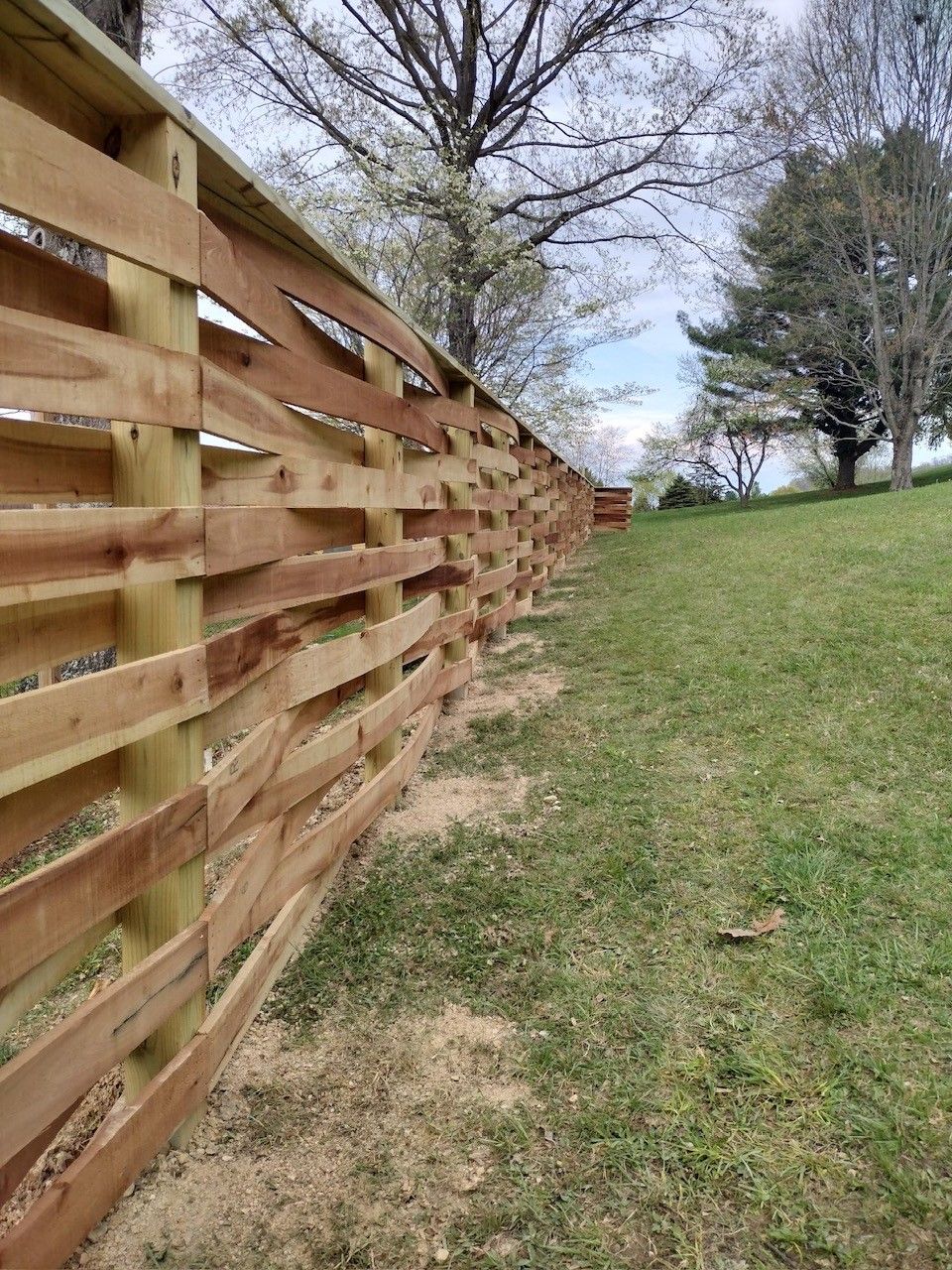 Wooden fence with alternating horizontal slats on a grassy hillside.