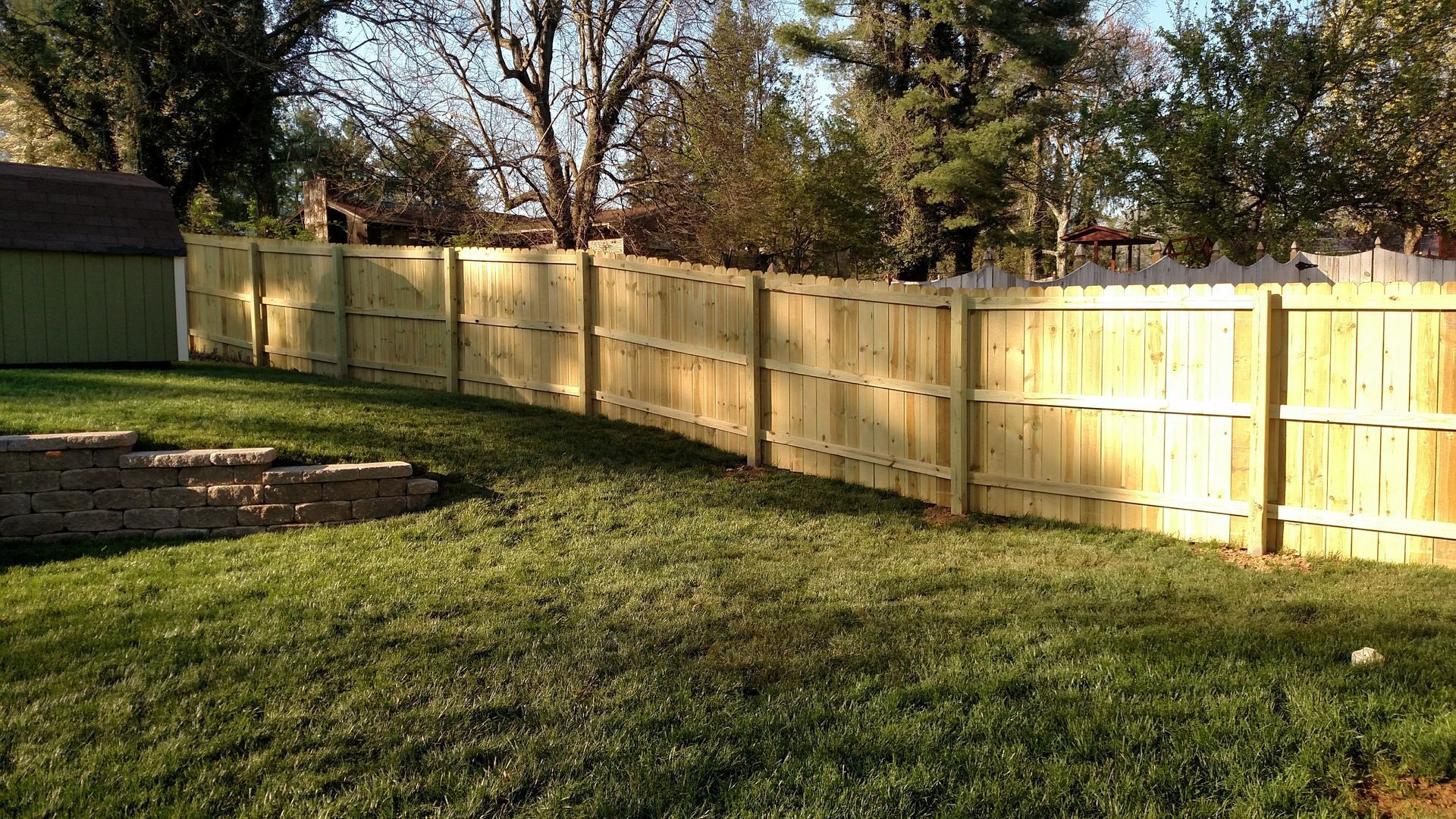 A wooden fence is in the middle of a lush green yard.