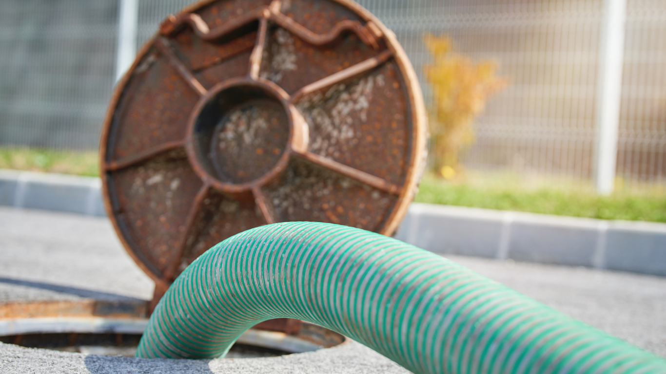 A green hose is coming out of a manhole cover.