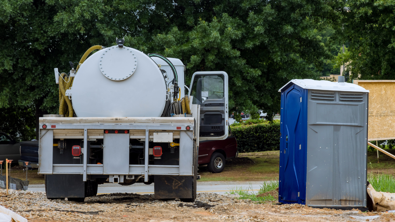 A vacuum truck is parked next to a blue portable toilet.