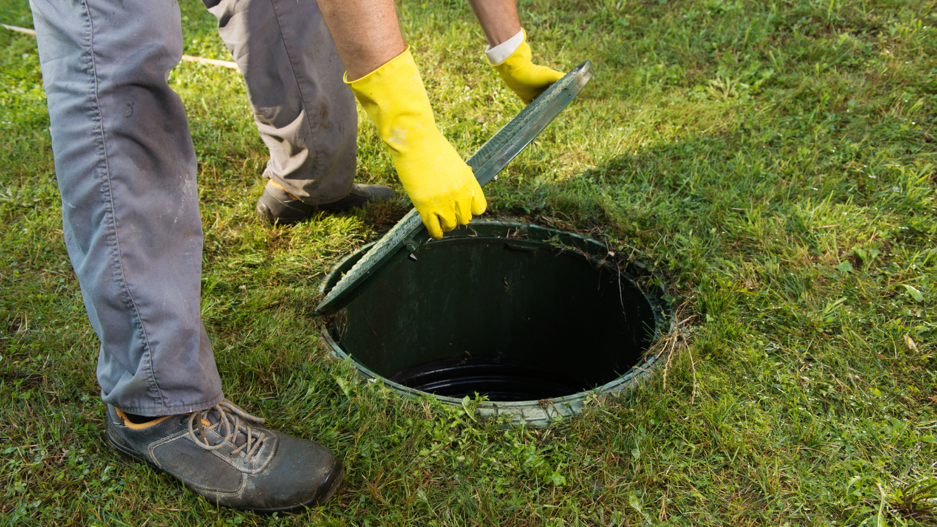 A person wearing yellow gloves is opening a septic tank.