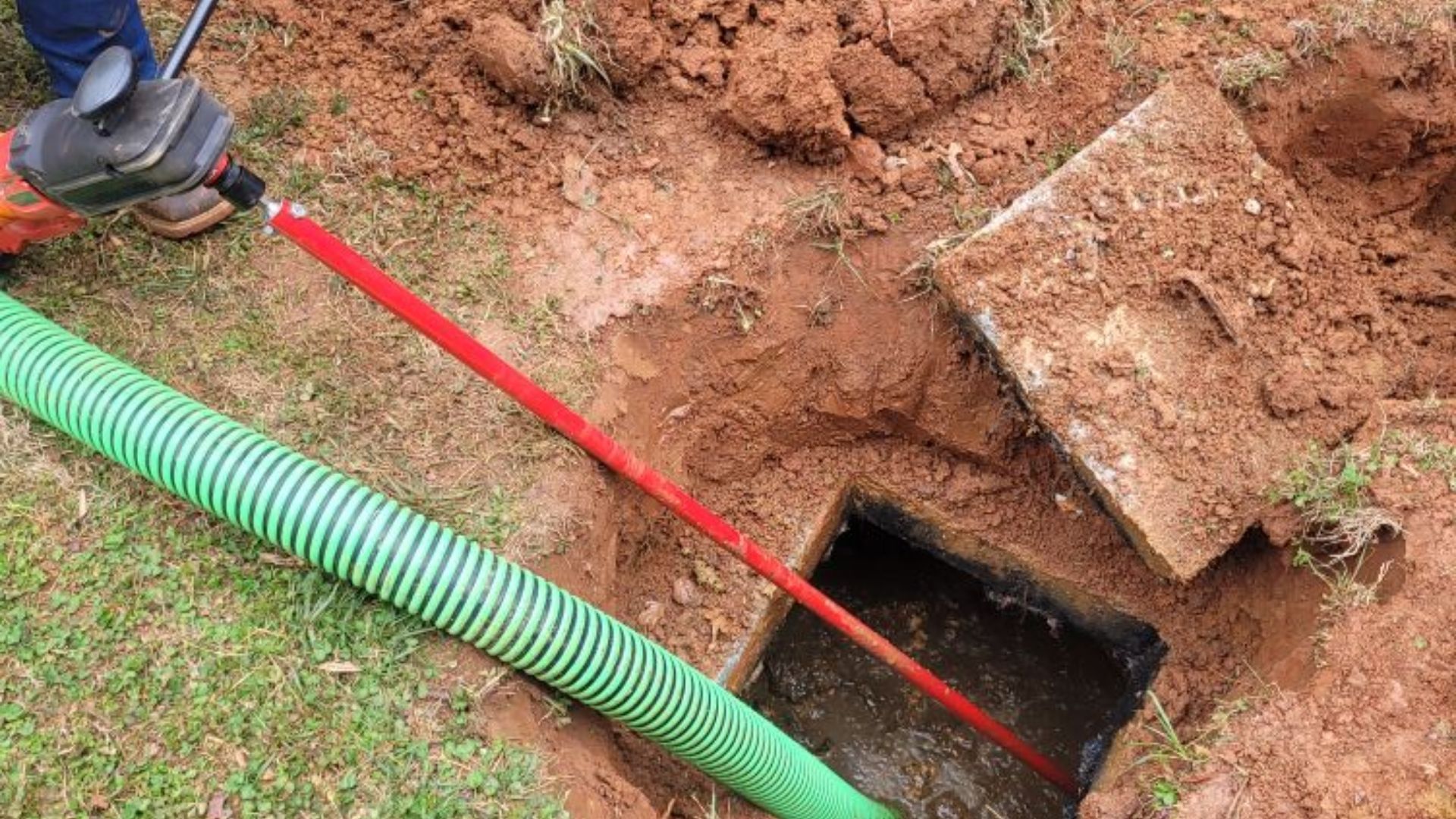 A person is using a green hose to drain a septic tank.