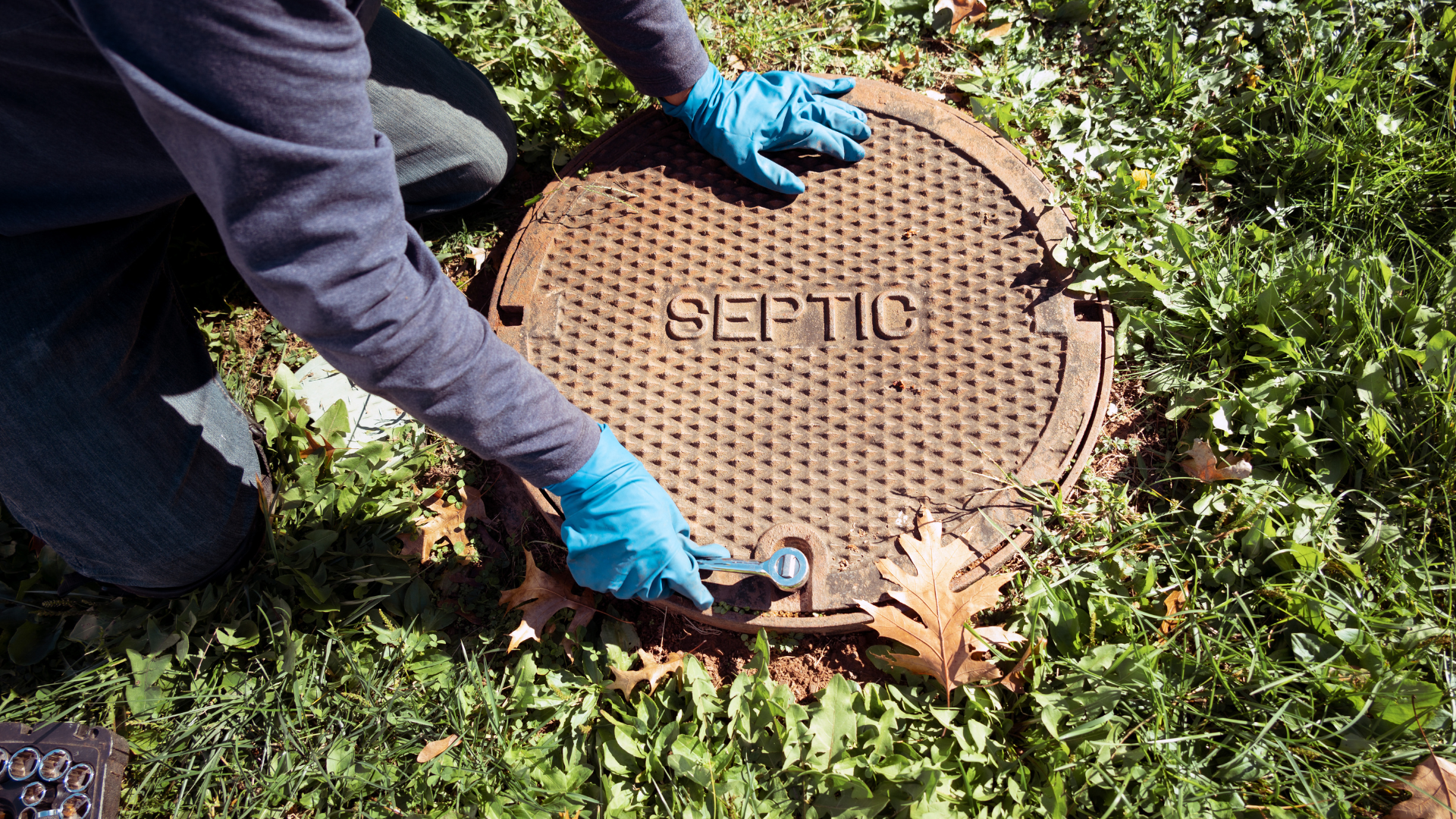 A person wearing blue gloves is opening a septic tank lid.
