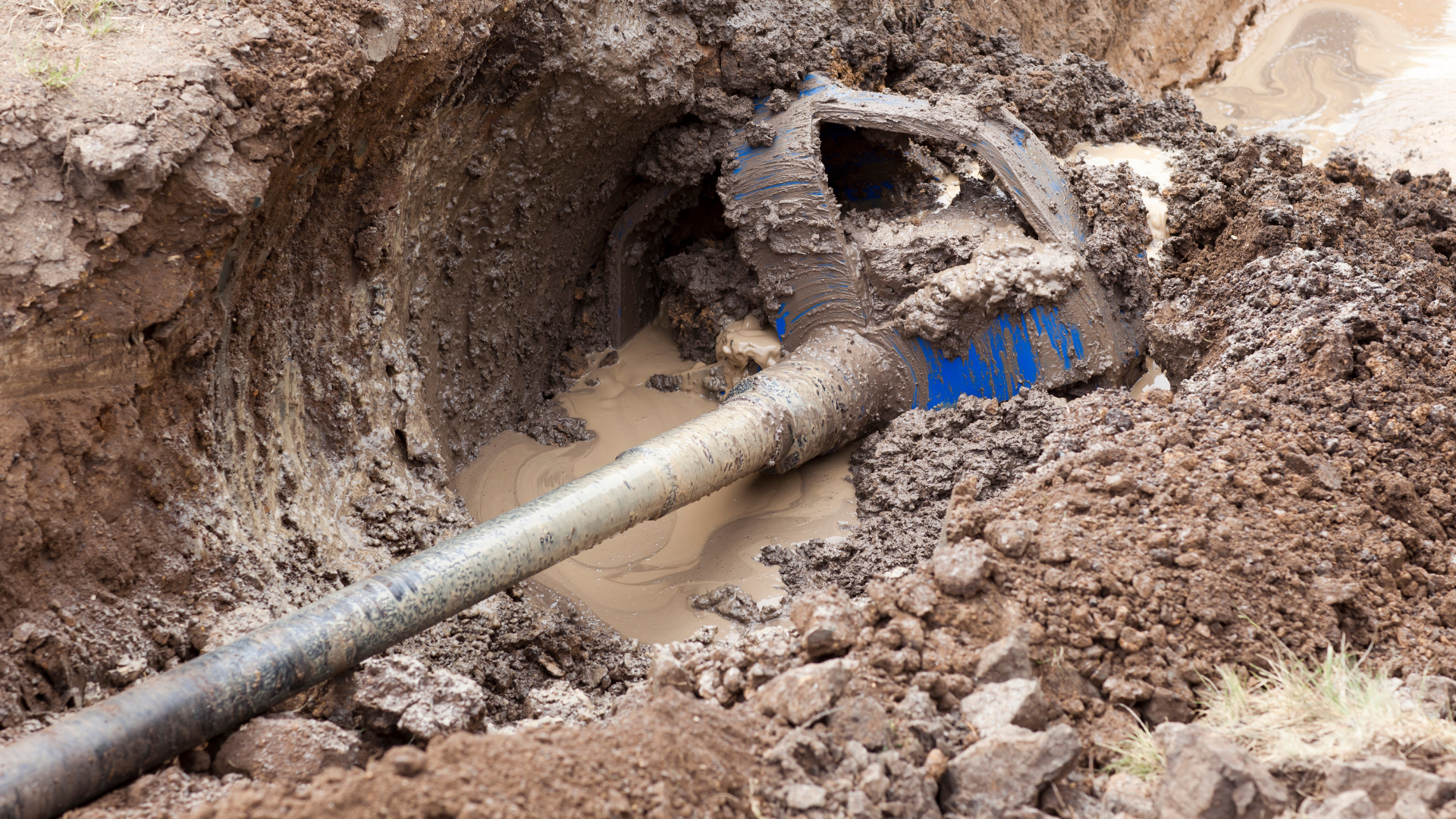 A muddy pipe is sticking out of a hole in the ground.