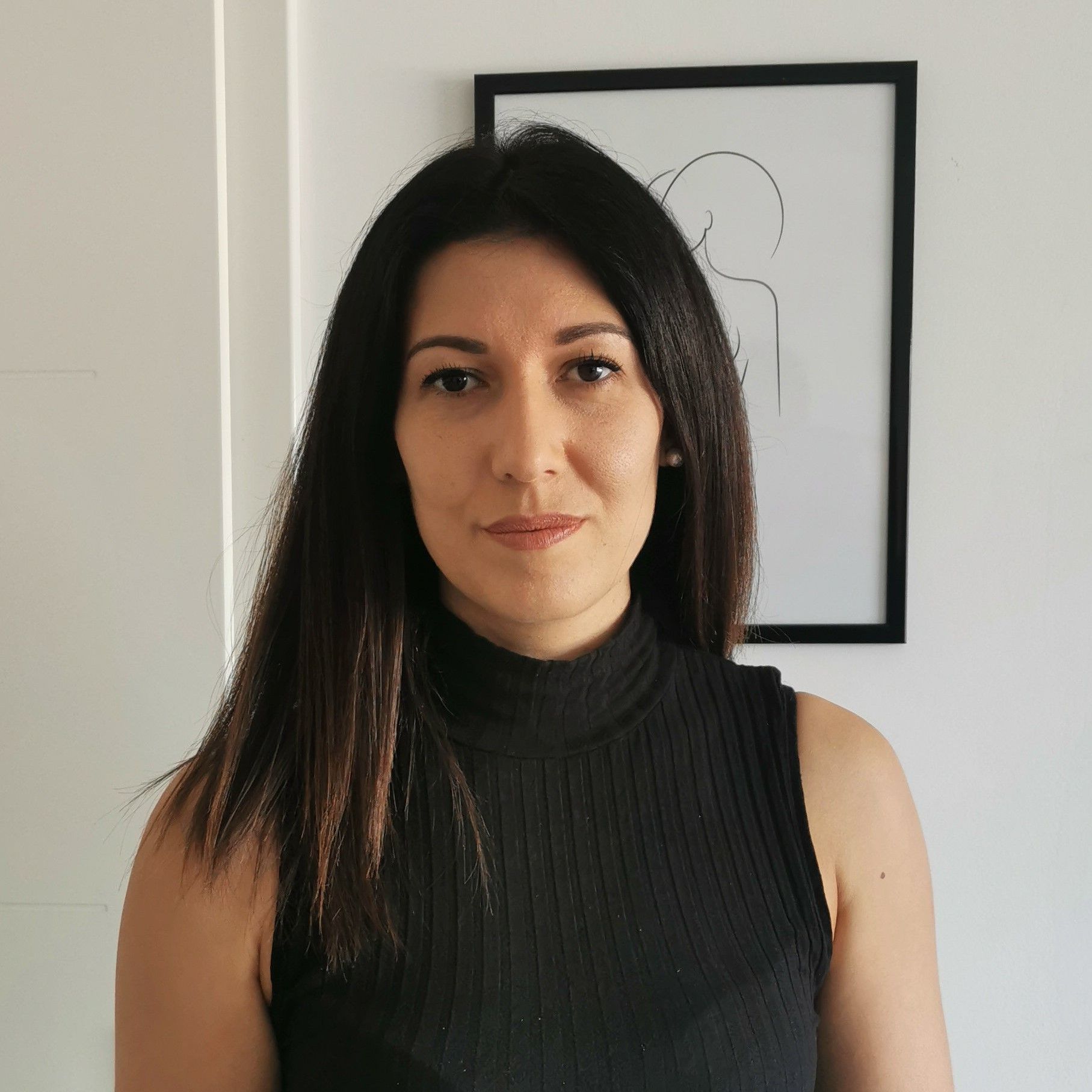 Une femme en débardeur noir se tient devant un tableau sur le mur.