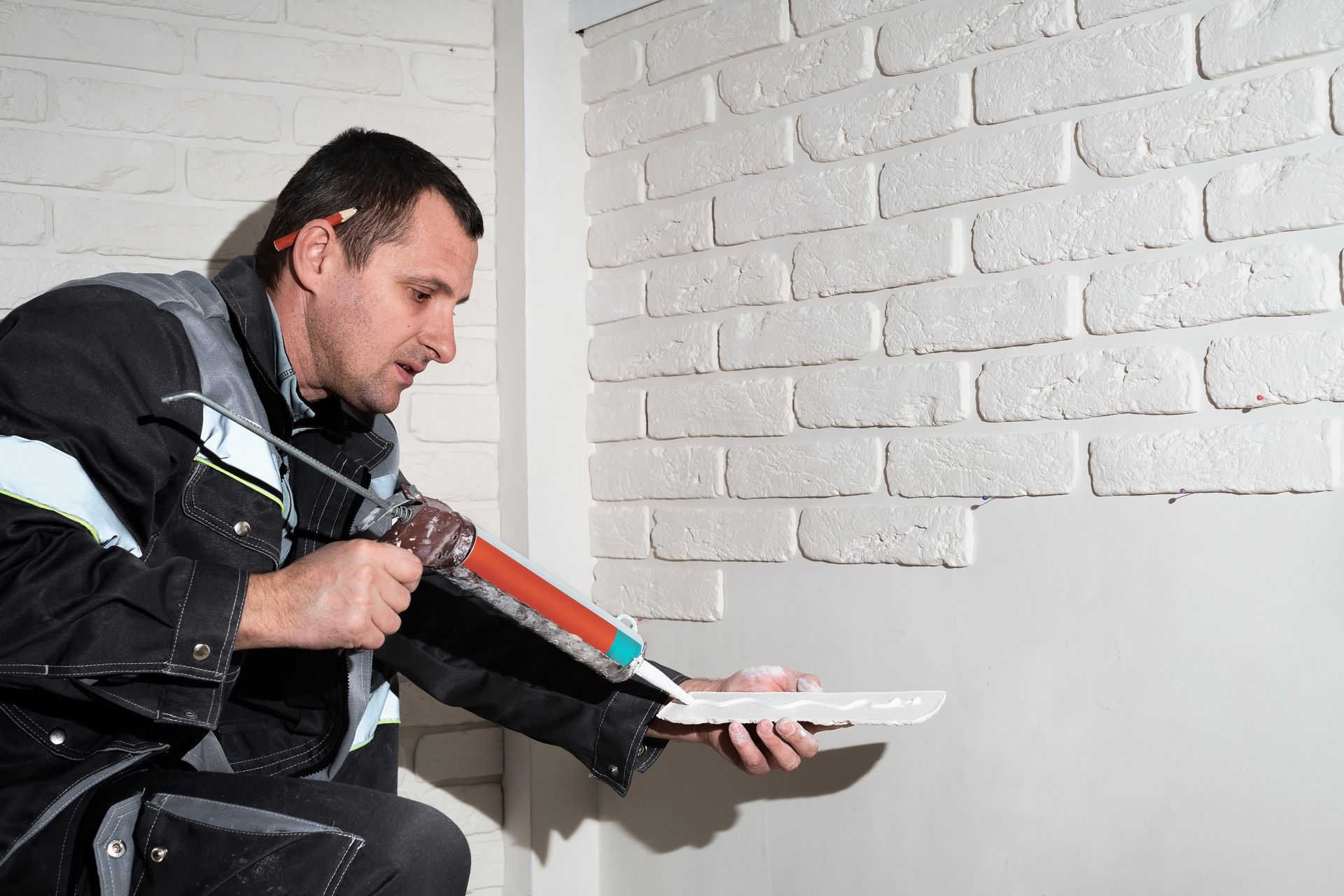 Un homme applique de la colle sur un mur de briques blanches.