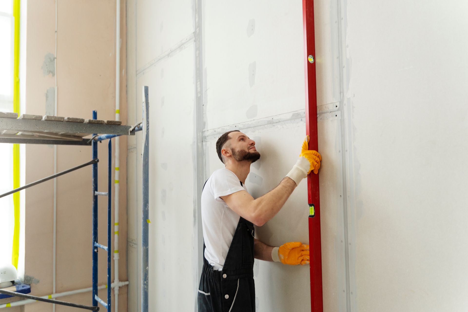 Un homme mesure un mur avec un niveau rouge.