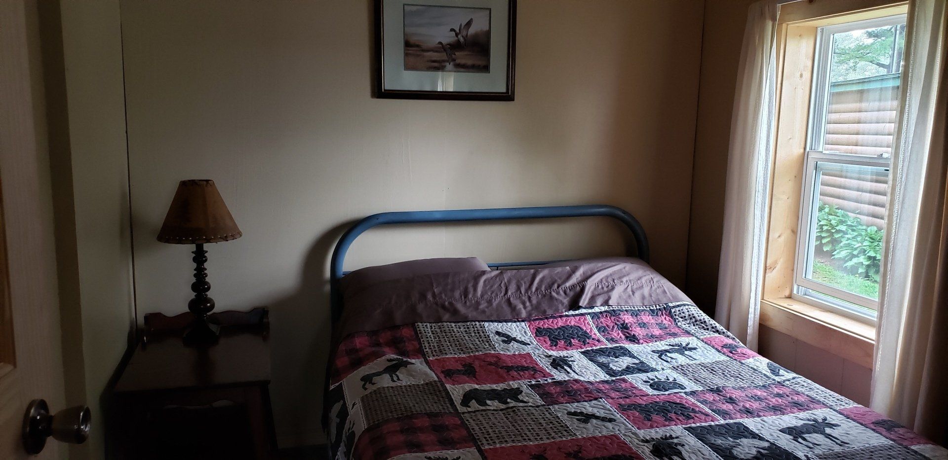A bedroom with a bed , nightstand , lamp and window.