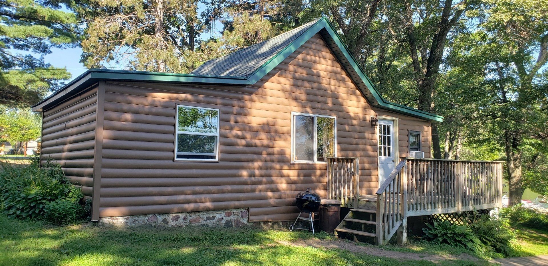 A small log cabin with a green roof and a deck.