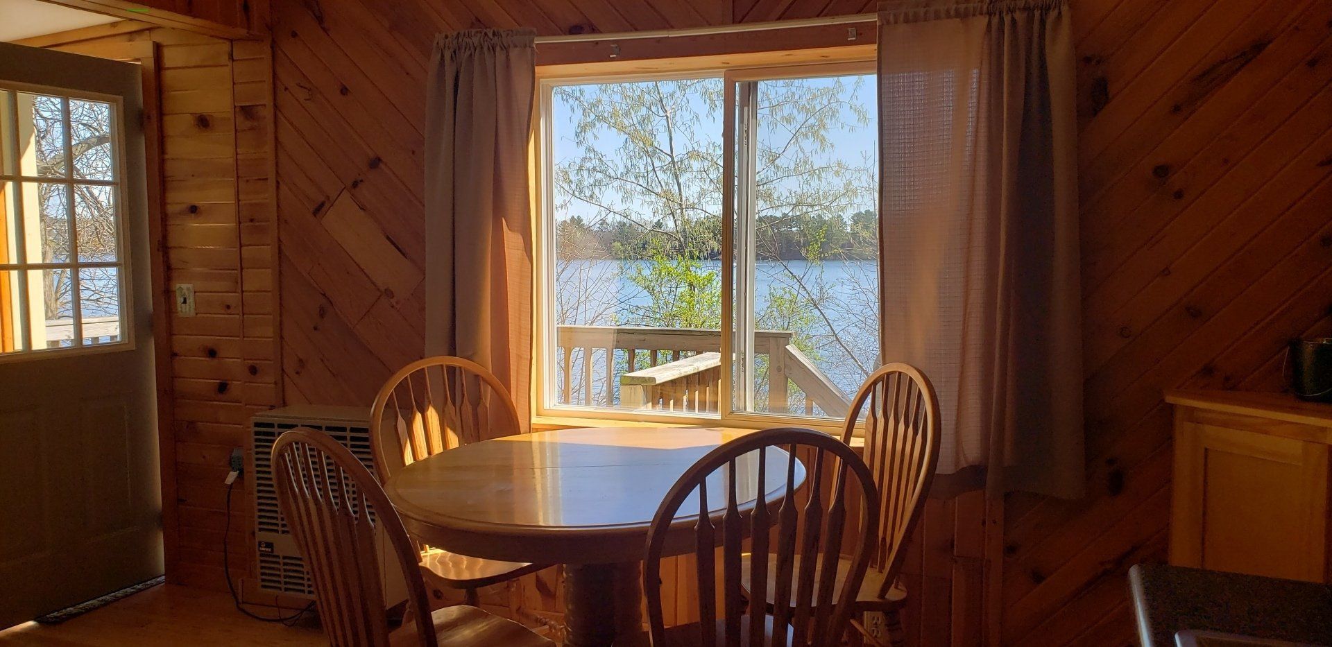 A wooden cabin with a table and chairs in front of a window overlooking a lake.
