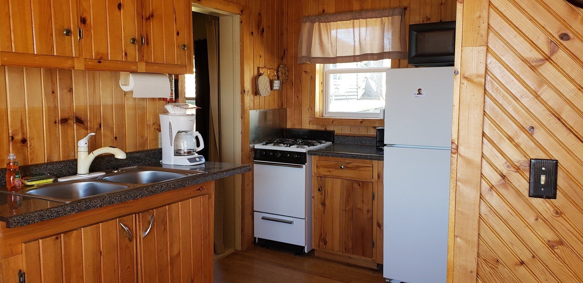 A kitchen with wooden cabinets , a sink , stove , refrigerator and microwave.