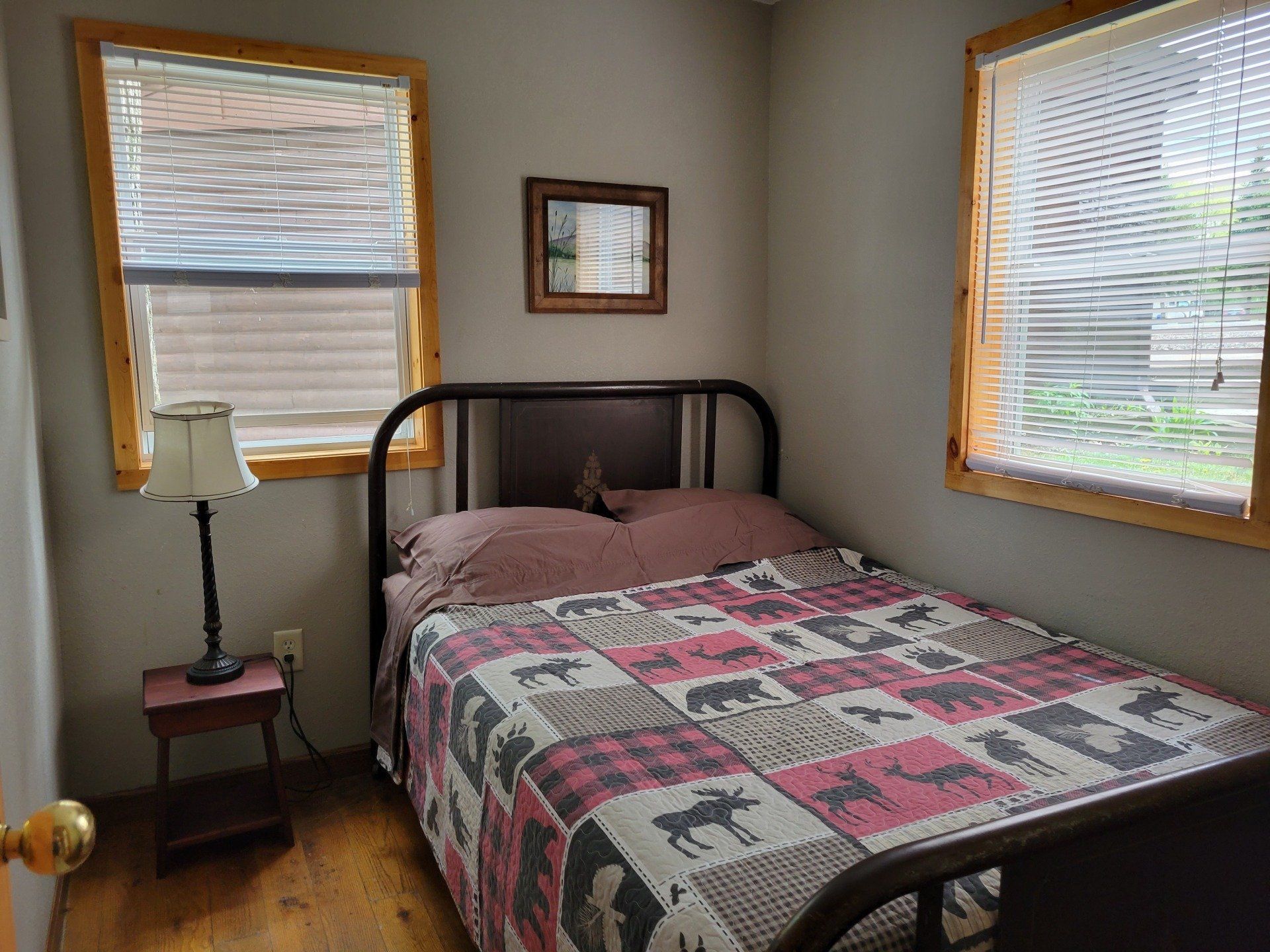 A bedroom with a bed , nightstand , lamp and two windows.