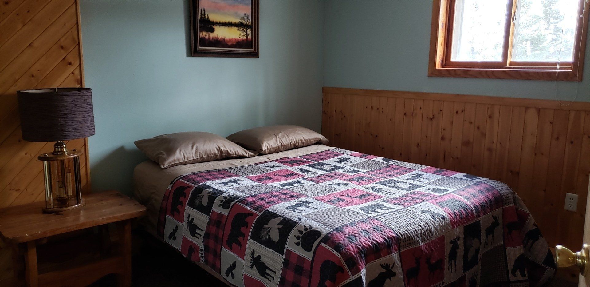 A bedroom with a bed , nightstand , lamp and window.