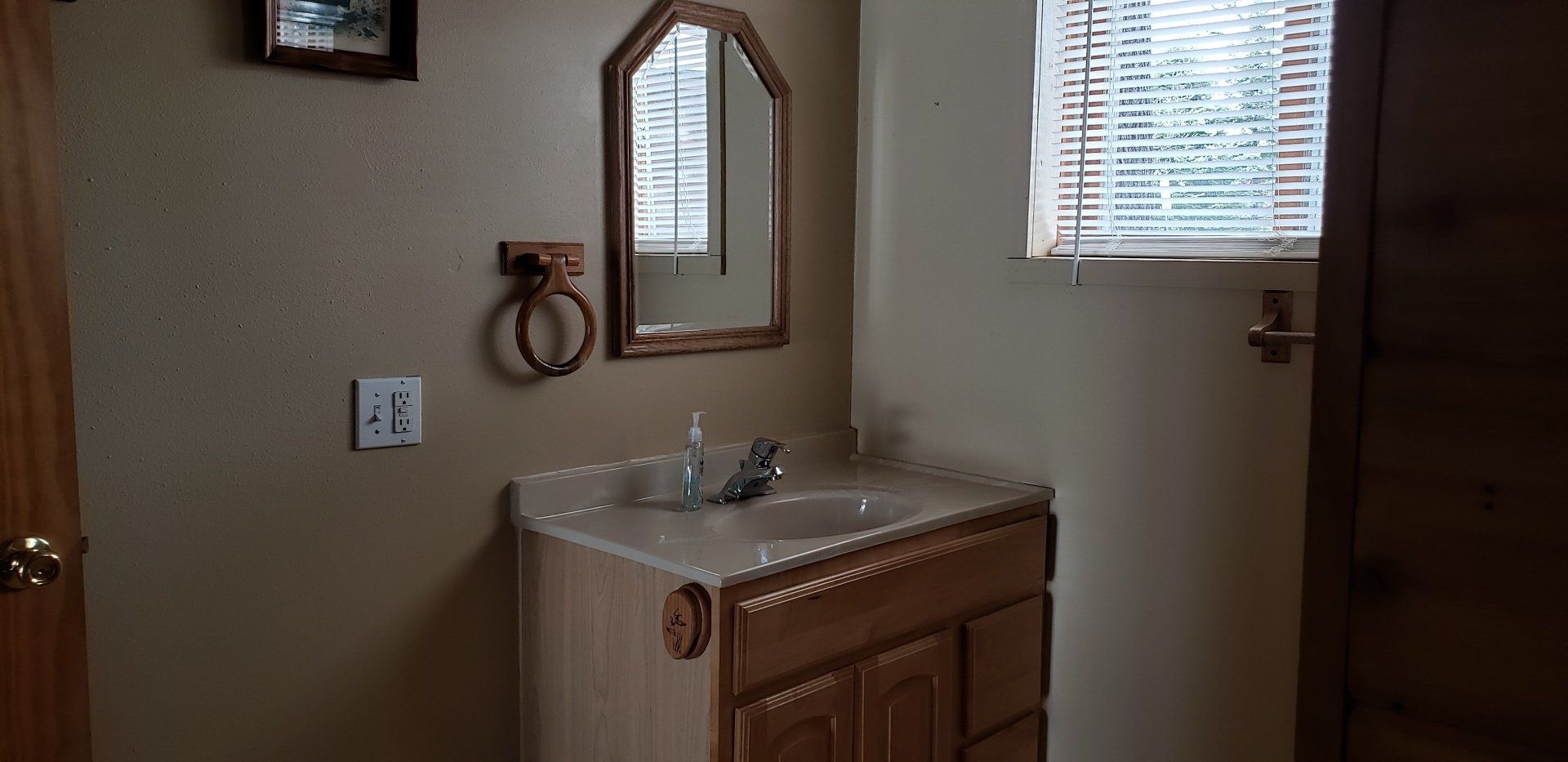 A bathroom with a sink , mirror and window.