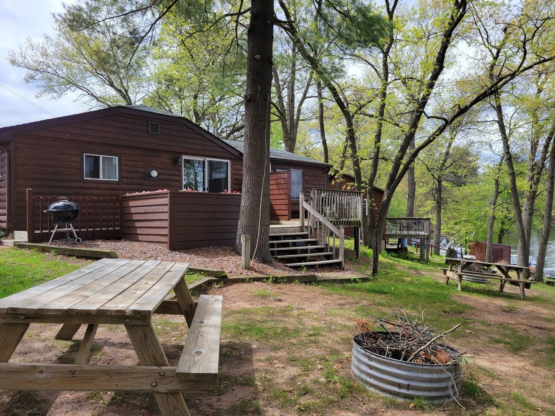 A wooden cabin with a picnic table and a fire pit in front of it.