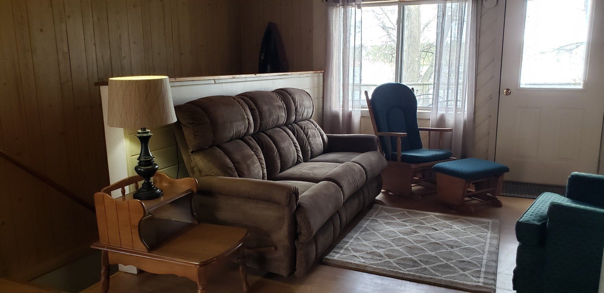 A living room with a couch , chair , lamp and stairs.