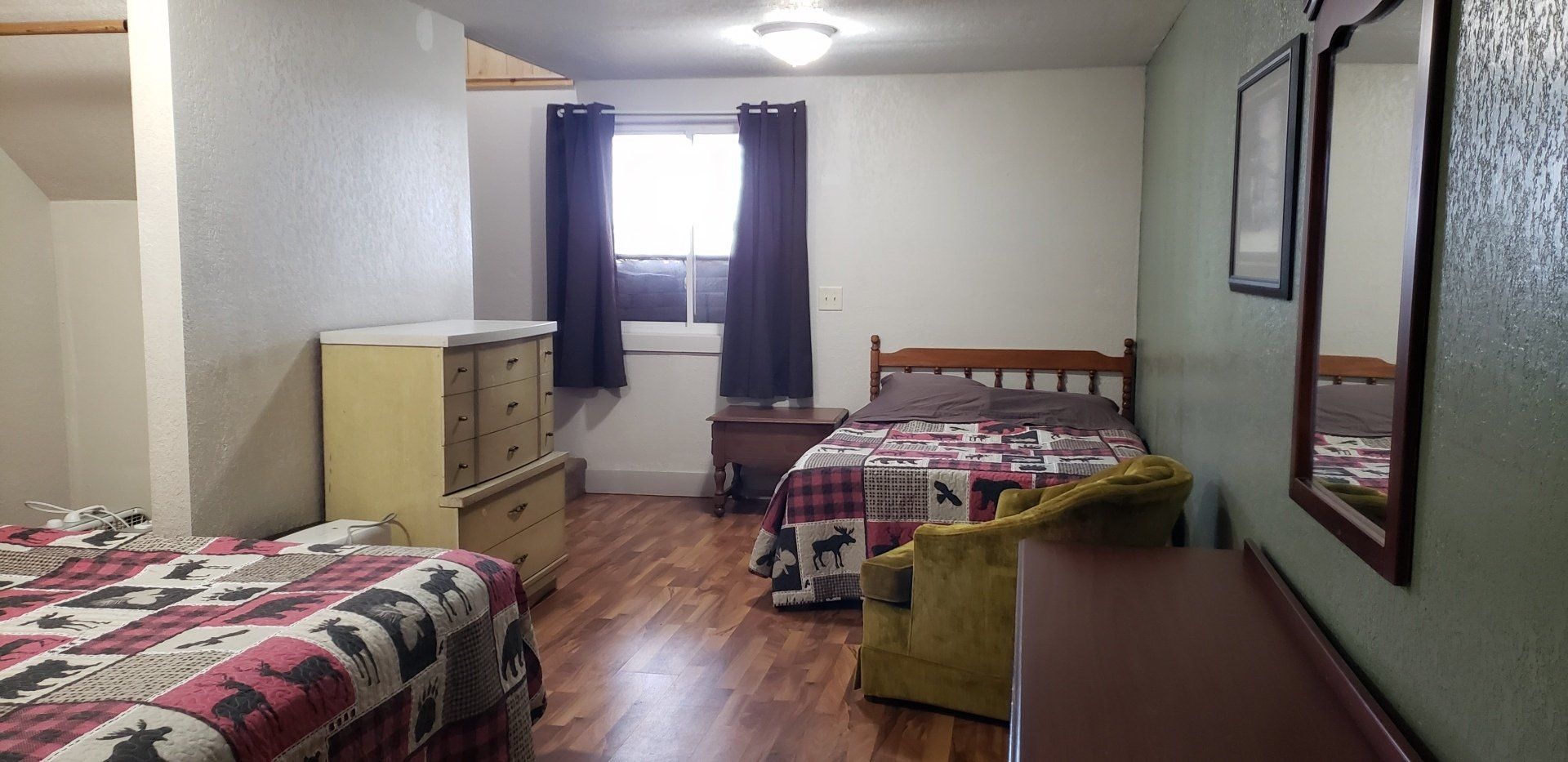 A bedroom with two beds , a dresser , a chair and a mirror.