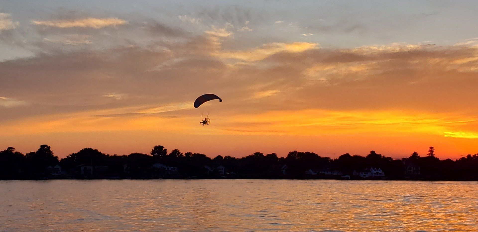 A person is parasailing over a lake at sunset.