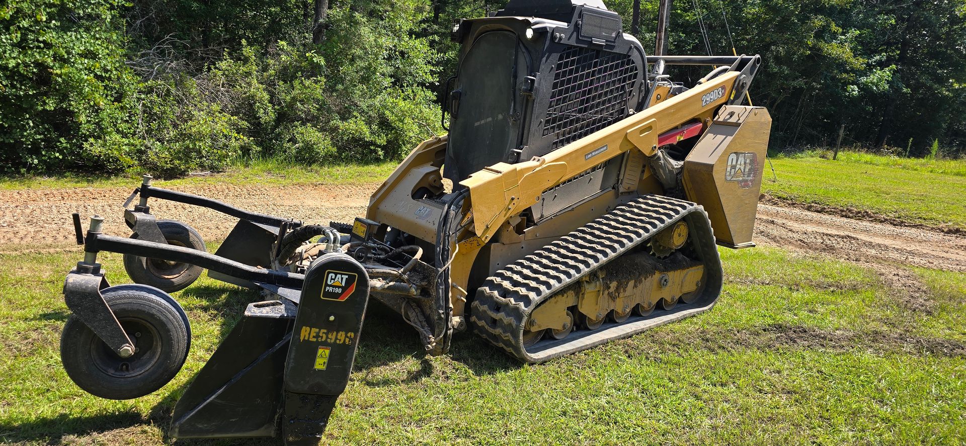 Yellow track loader with mower attachment on a grassy area.