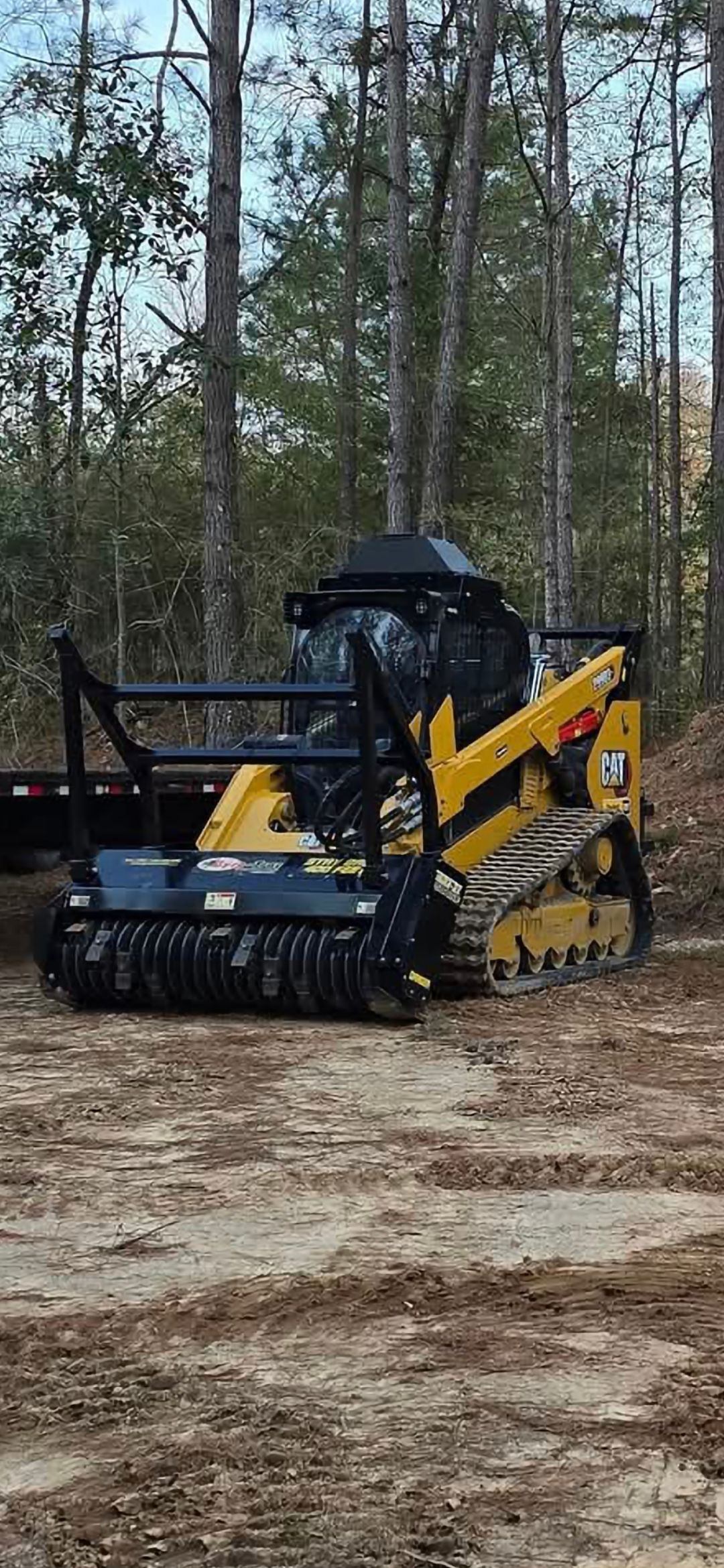 Yellow and black tracked mulcher in a wooded area.