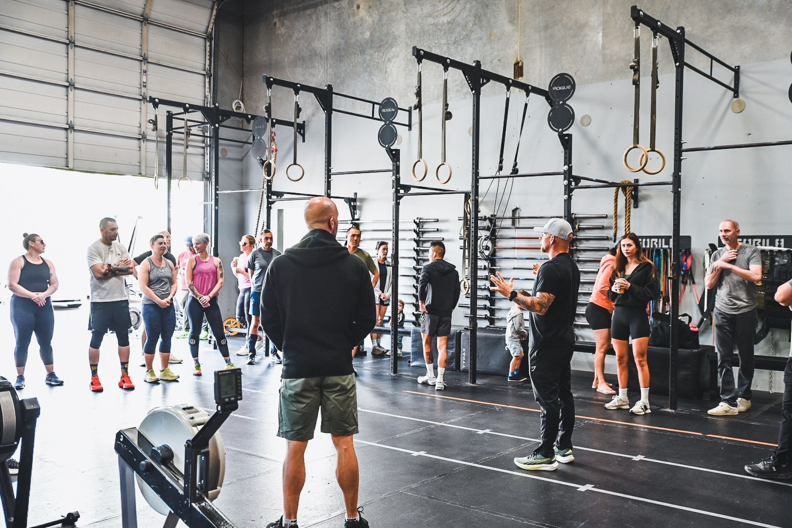 People exercising in a gym around rowing machines, with a coach walking by.