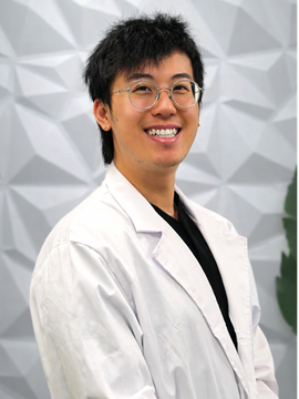 A professional in a white lab coat and glasses smiling against a textured, light-colored geometric background.