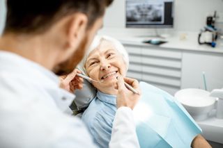 Dentist examining patient's teeth in a dental office. Another assistant nearby. Both wearing masks and gloves.