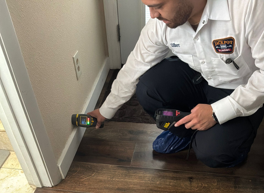 Technician kneeling and checking a wall for moisture with a handheld testing device in a hallway.