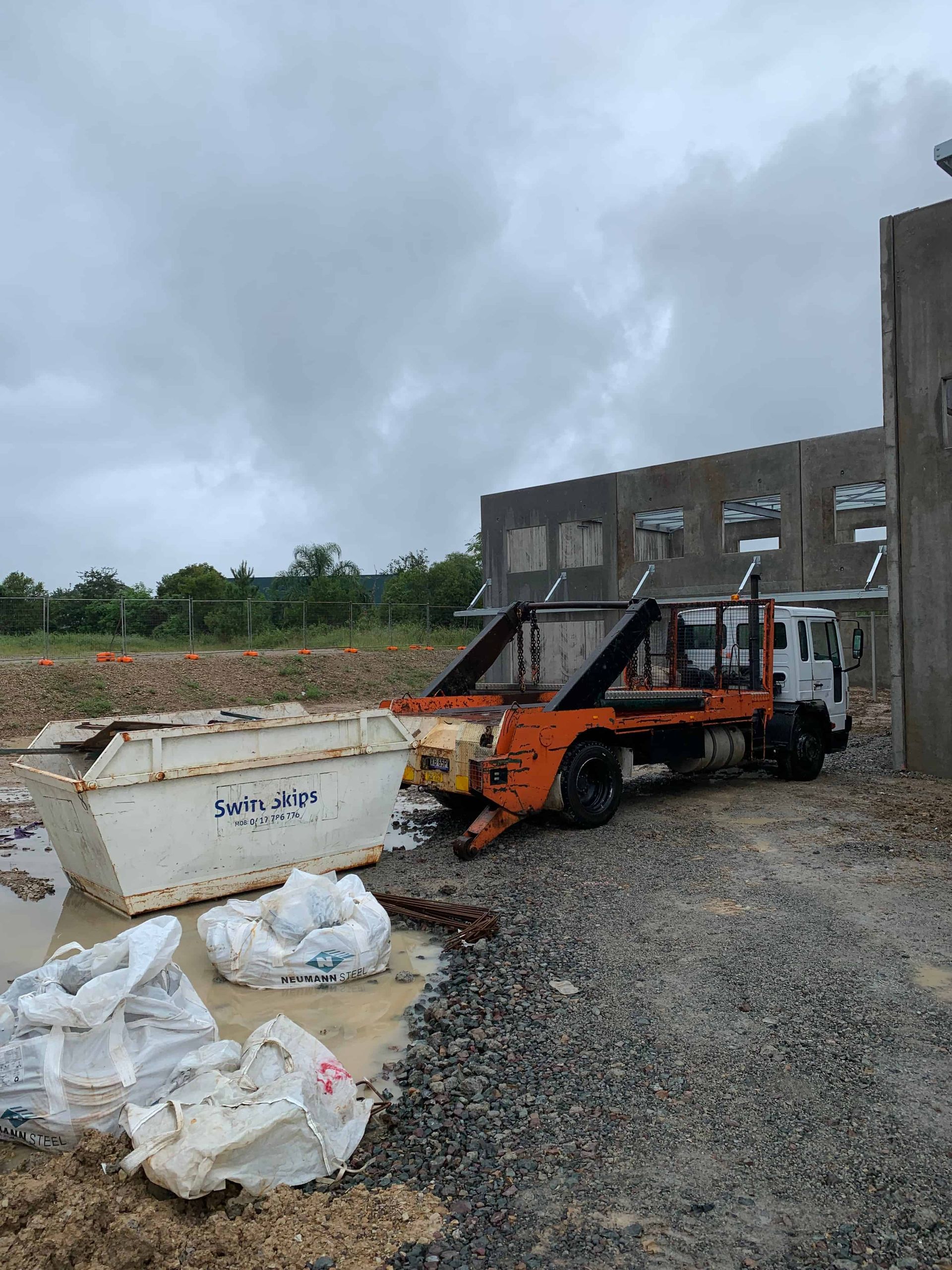 Construction site with skip truck lifting a large waste container, cloudy sky. — Swift Skips in Cooroy, QLD