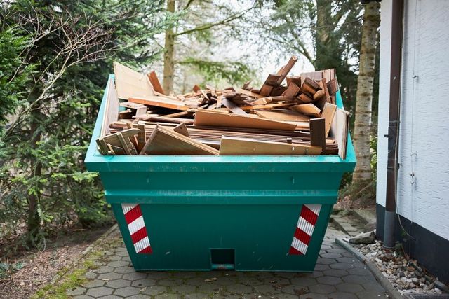 A Green Dumpster Filled With Wood Is Parked In Front Of A Building — Swift Skips in Gympie, QLD