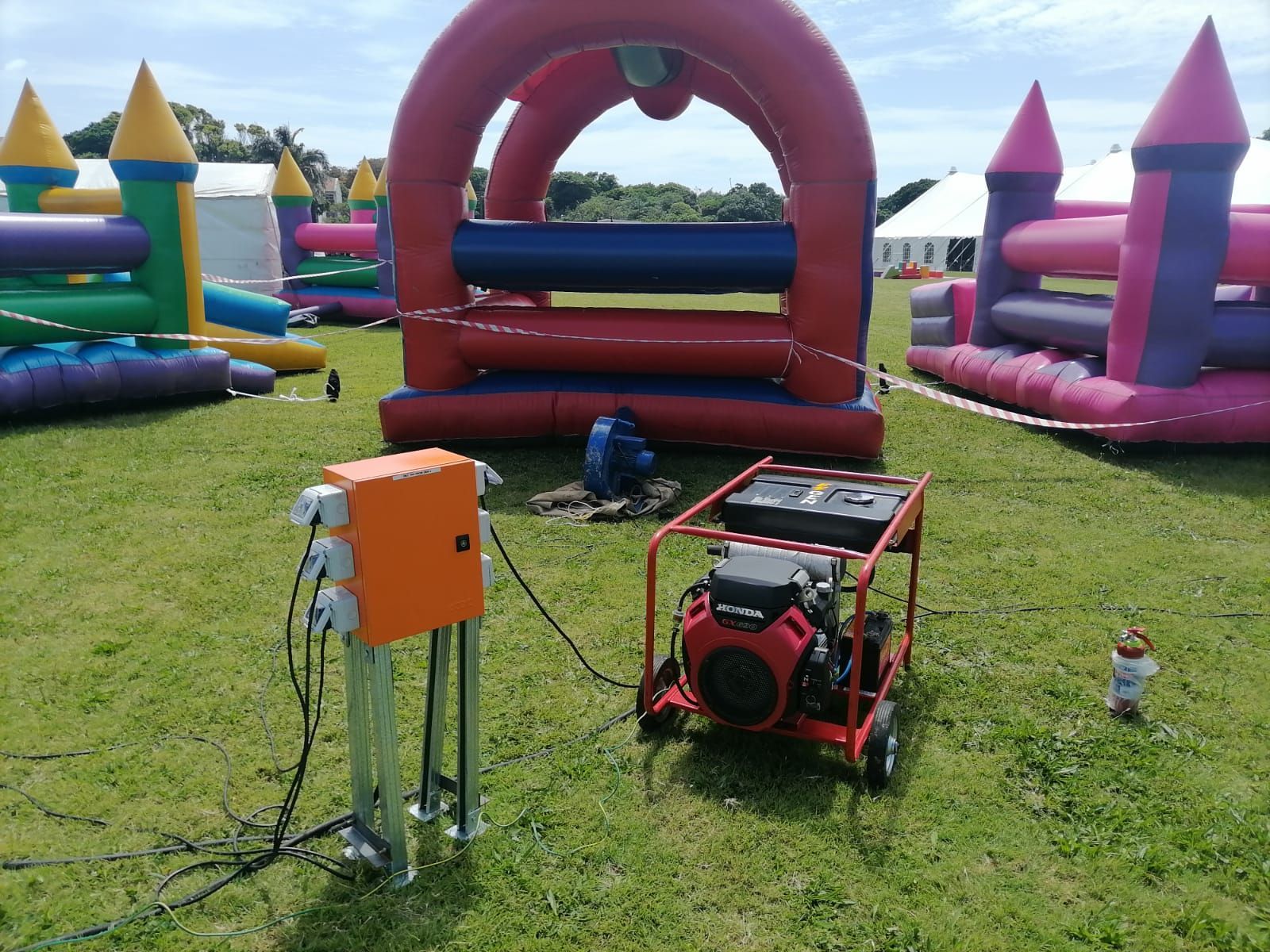 A generator is sitting in the grass in front of a bouncy house.