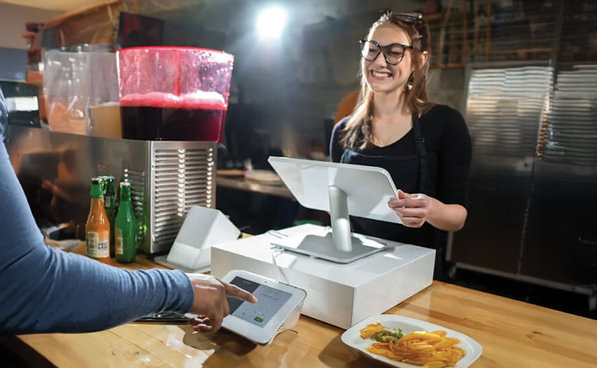 Barista smiling behind café register, serving a customer at a counter with drinks and pastries