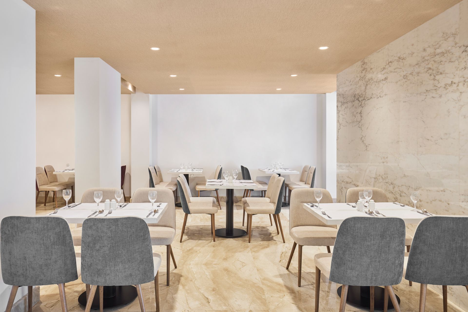 Modern restaurant dining room with set tables, gray chairs, and warm wood-and-white minimalist decor