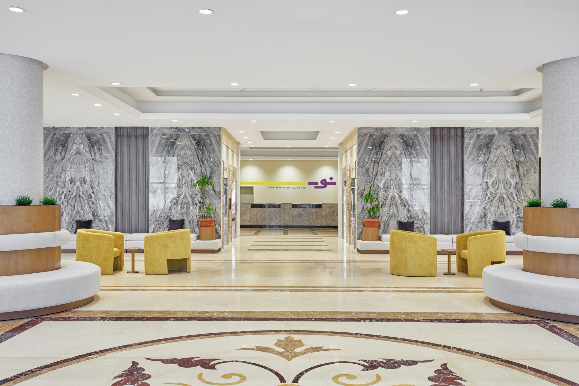 Bright hotel lobby with marble floors, yellow chairs, and decorative columns around a central reception area