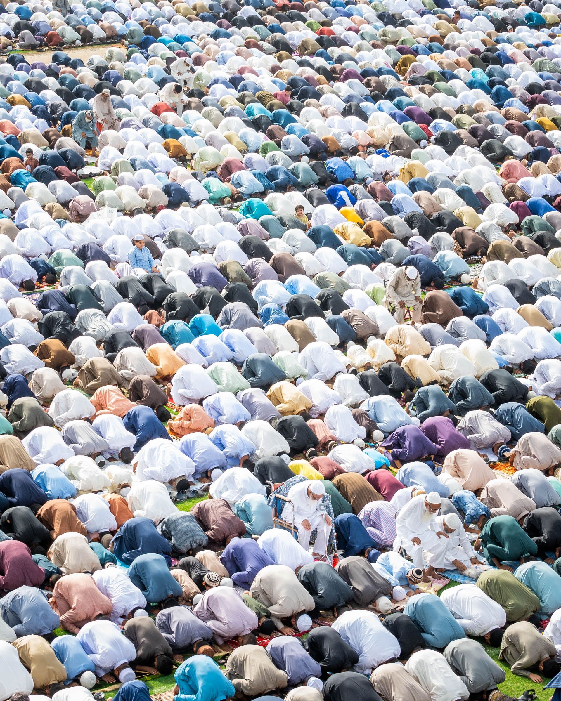Crowded group of people in white, blue, and colorful clothing, viewed from above in a dense outdoor gathering