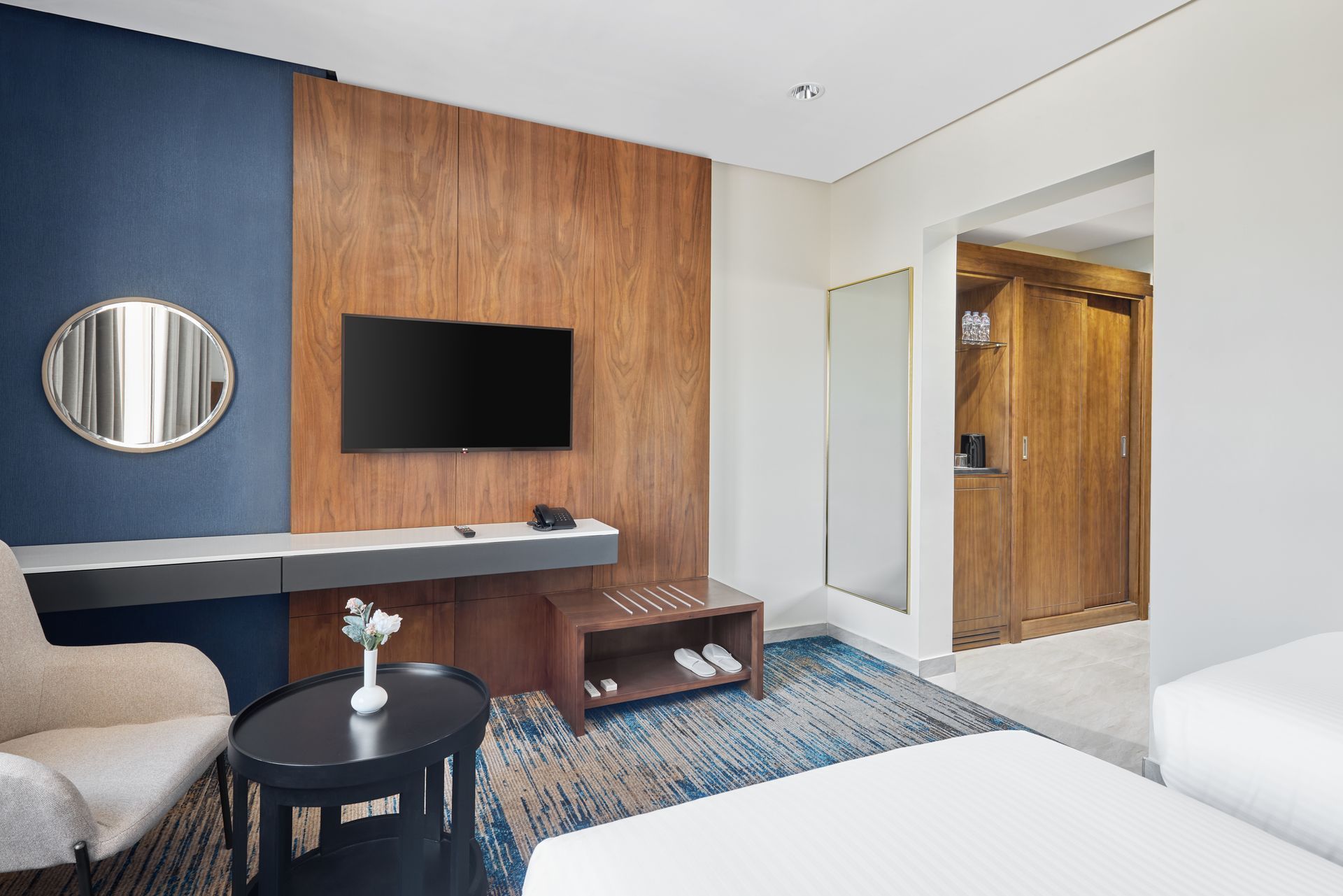 Modern hotel room with wall-mounted TV, desk, round mirror, and open bathroom area