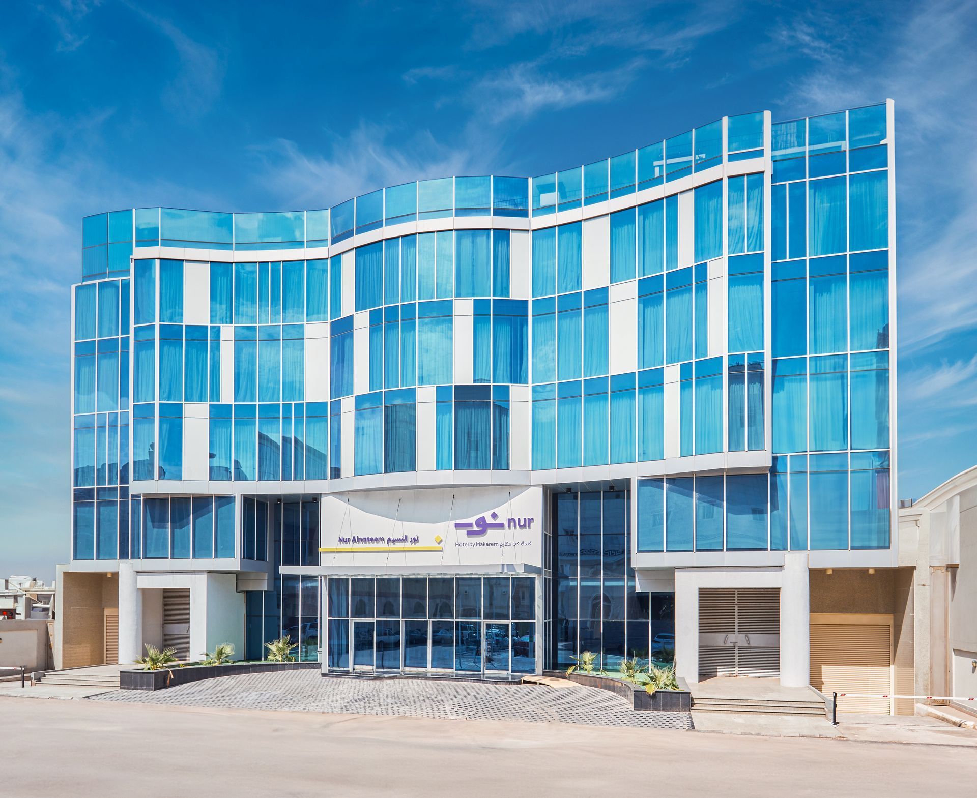 Modern blue-glass office building with a central entrance and parking area