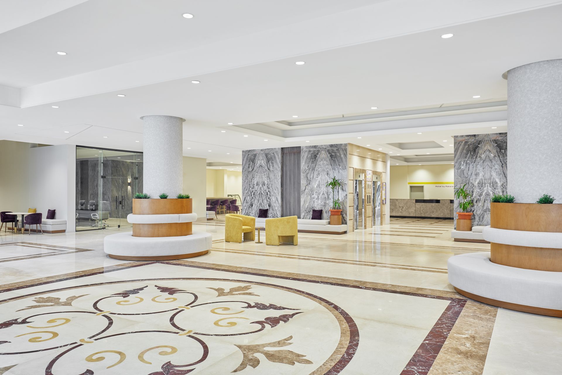 Bright hotel lobby with white marble floors, circular seating, and patterned carpet accents