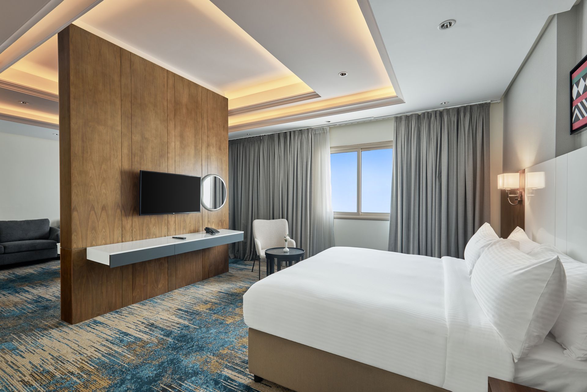 Modern hotel room with two beds, wall-mounted TV, blue patterned carpet, and window with curtains