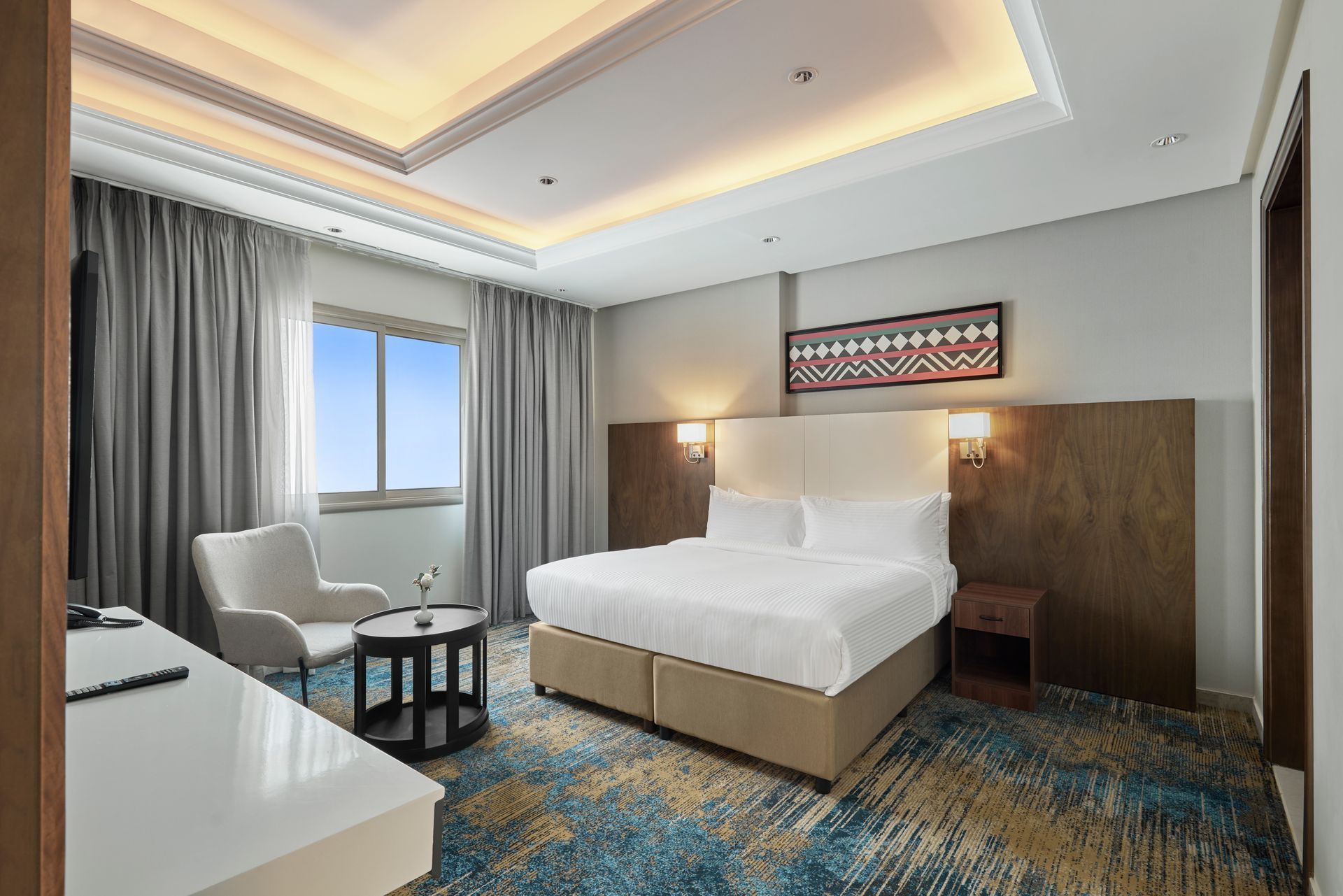 Modern hotel room with a bed, armchair, window, and warm ambient lighting