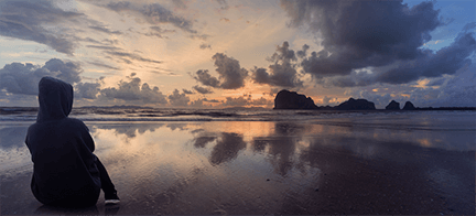 A person is sitting on the beach looking at the sunset.