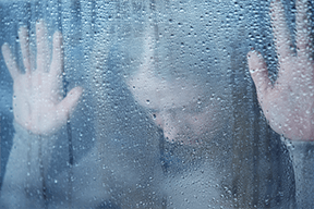 A woman is behind a window with her hands on it.