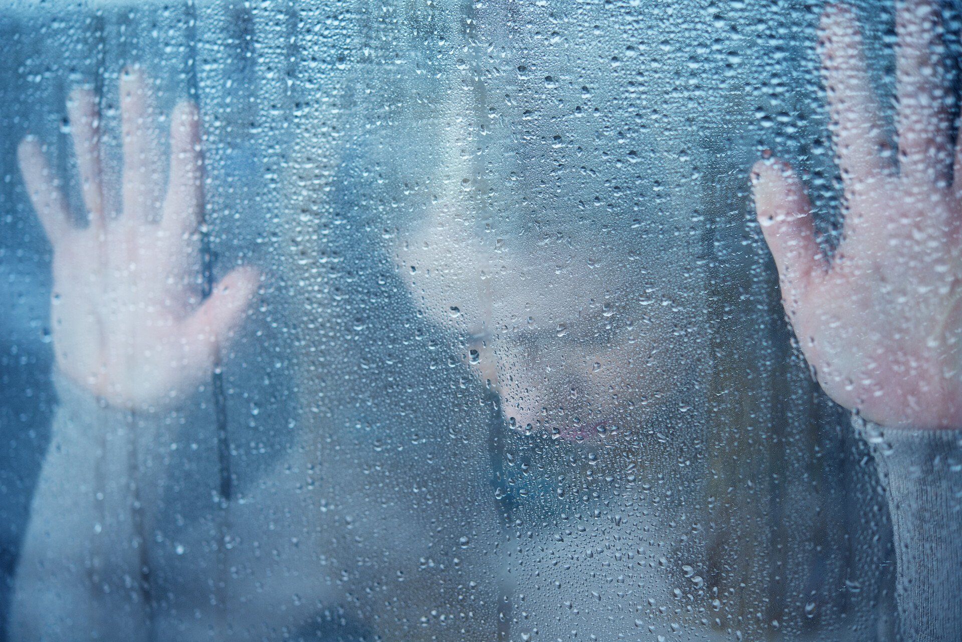 A woman is behind a window with her hands on it.